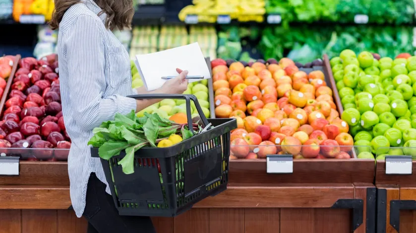 A woman with a basket and a grocery list browses colorful apples at the supermarket